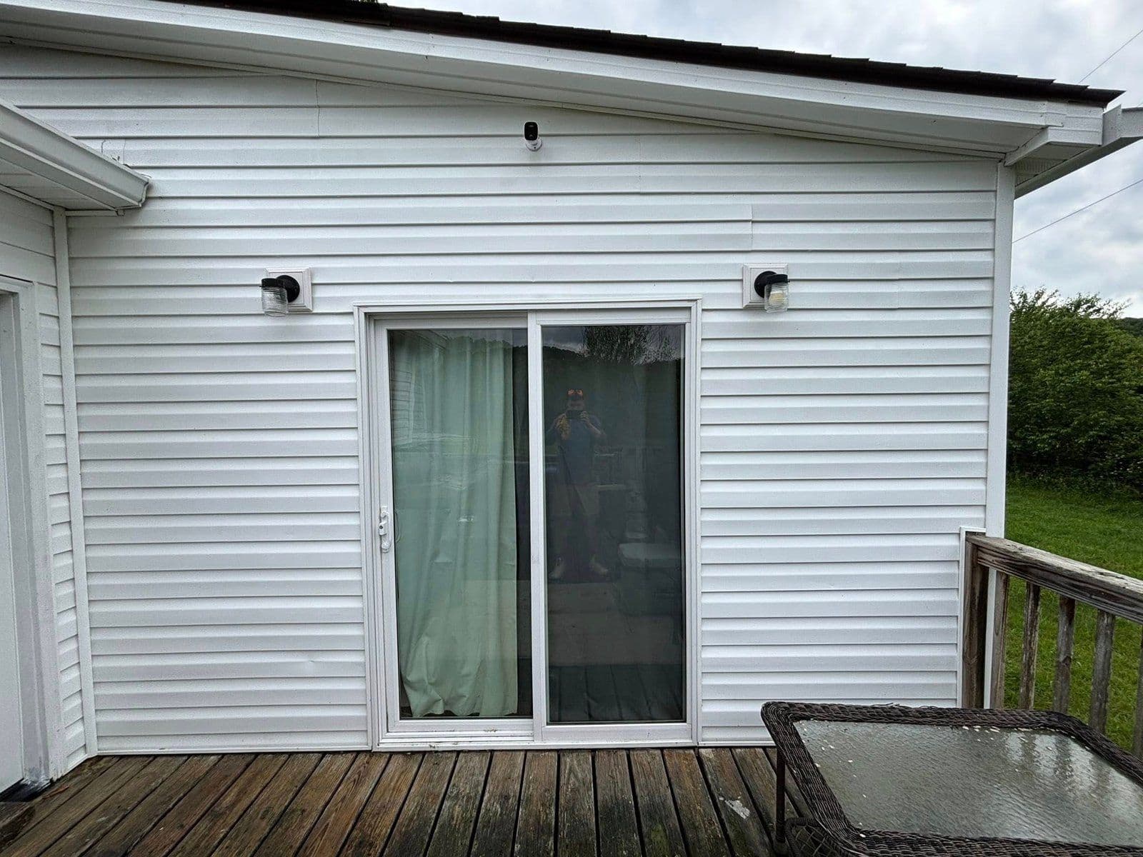 Exterior view of a house with double sliding doors and wall-mounted lights on siding.