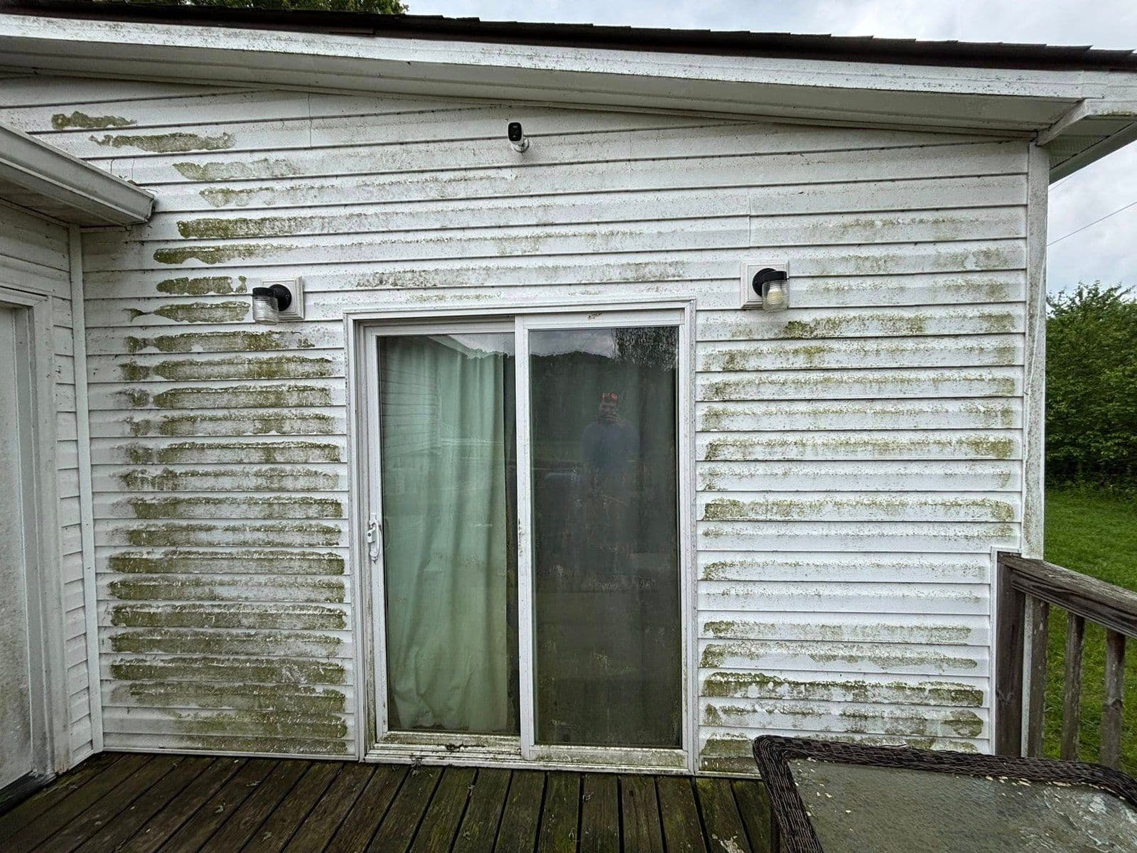Moldy exterior wall and sliding glass door with dirty curtains on a wooden deck.