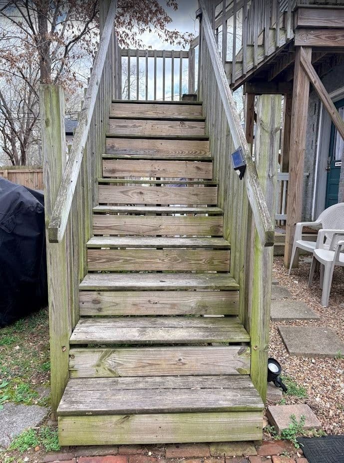 Weathered wooden stairs leading up to a deck in a residential backyard setting.