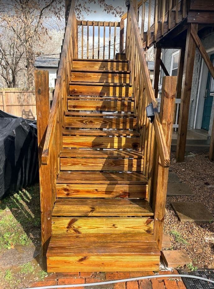 Sturdy wooden stairs with natural finish leading to a house, surrounded by grass and gravel.