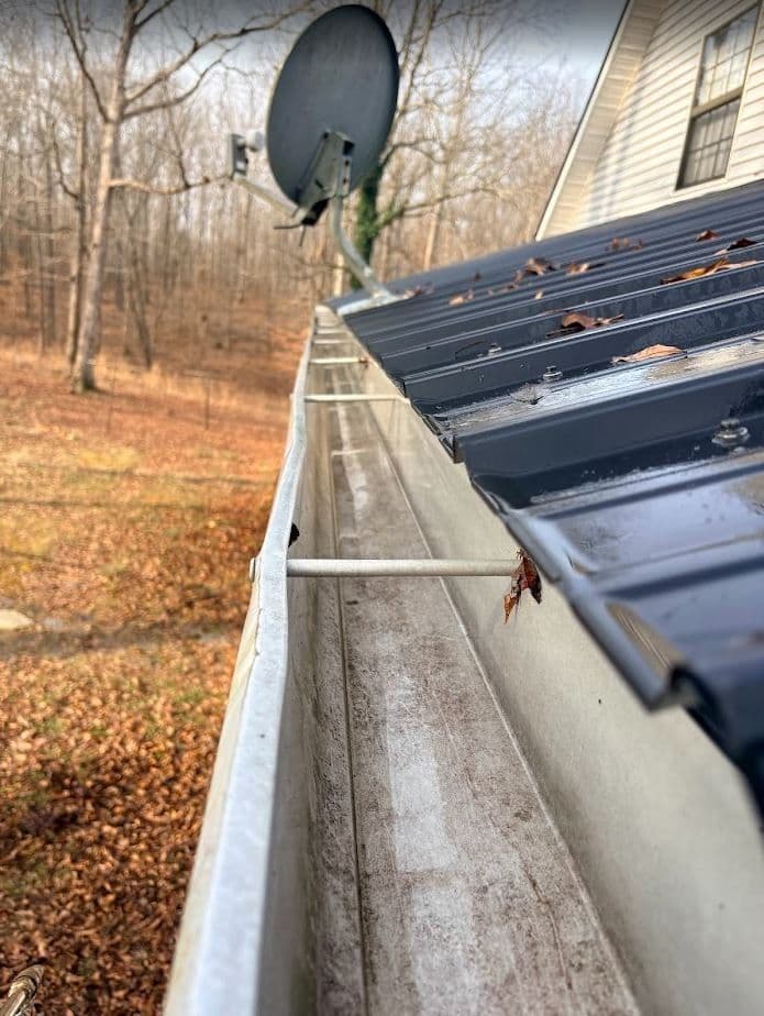 Gutters with leaves and debris on a metal roof, satellite dish in background, autumn setting.